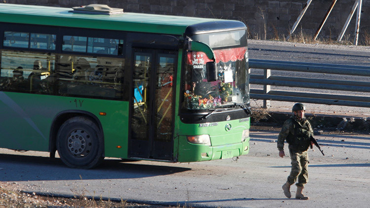 Un autobús que evacúa vecinos de Alepo oriental pasa junto a un miembro de las fuerzas leales al Gobierno sirio, el 15 de diciembre de 2016