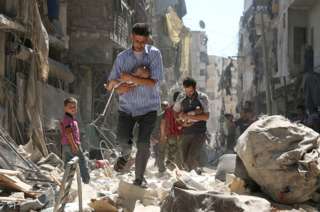 Hombres sirios cargando bebés entre los escombros de edificios en Alepo, 11 de septiembre de 2016.