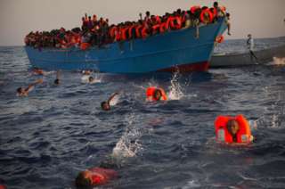 Migrantes saltando de un bote de madera atiborrado de gente para recibir la ayuda de una ONG durante una operación de rescate en el mar Mediterráneo el 29 de agosto 2016.