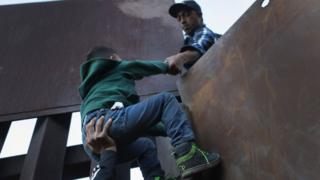 A boy is hoisted by fellow members of the migrant caravan over the US-Mexico border fence