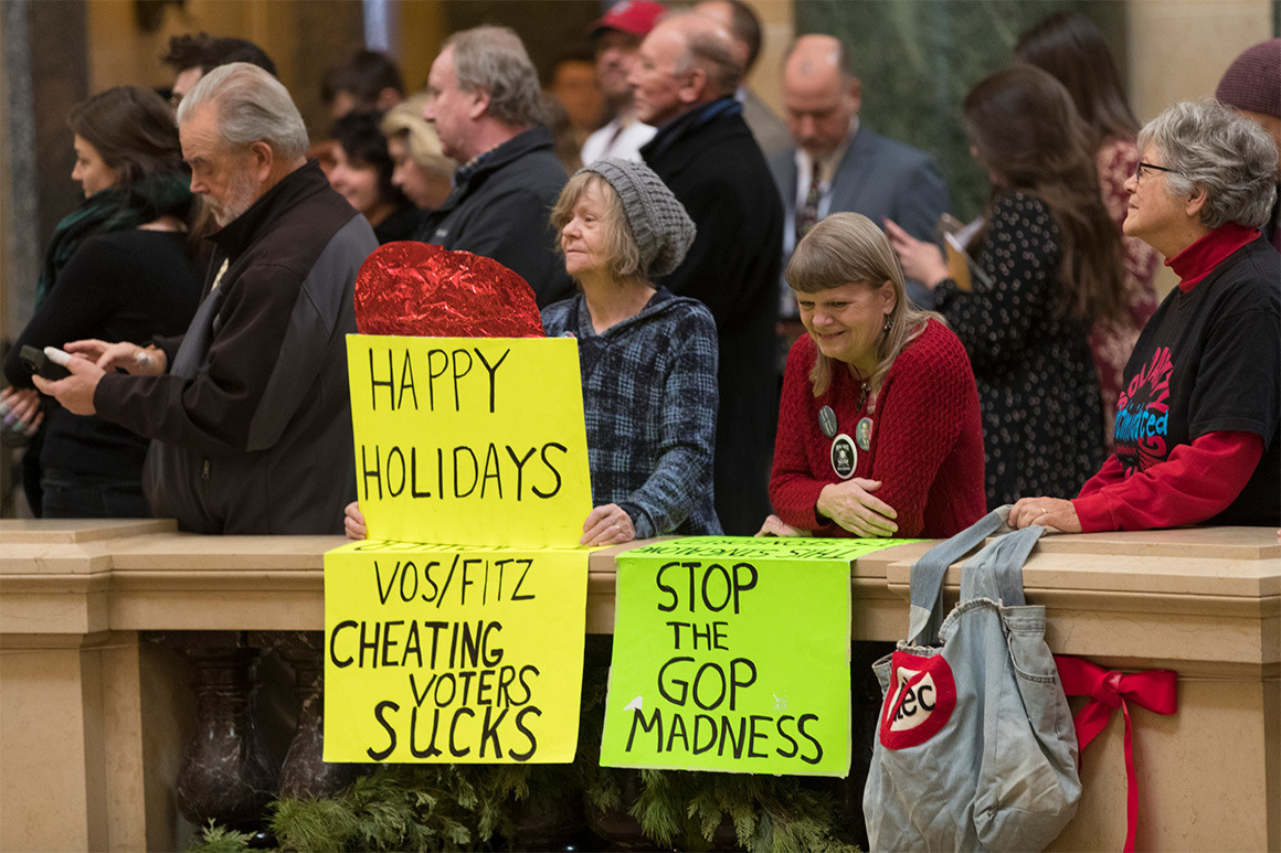 Protesters hold signs in the Wisconsin state capitol while demonstrating against the lame-duck session